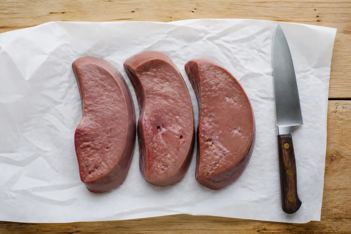 Tranches épaisses de foie de veau posées sur un papier de boucher sur un plan de travail