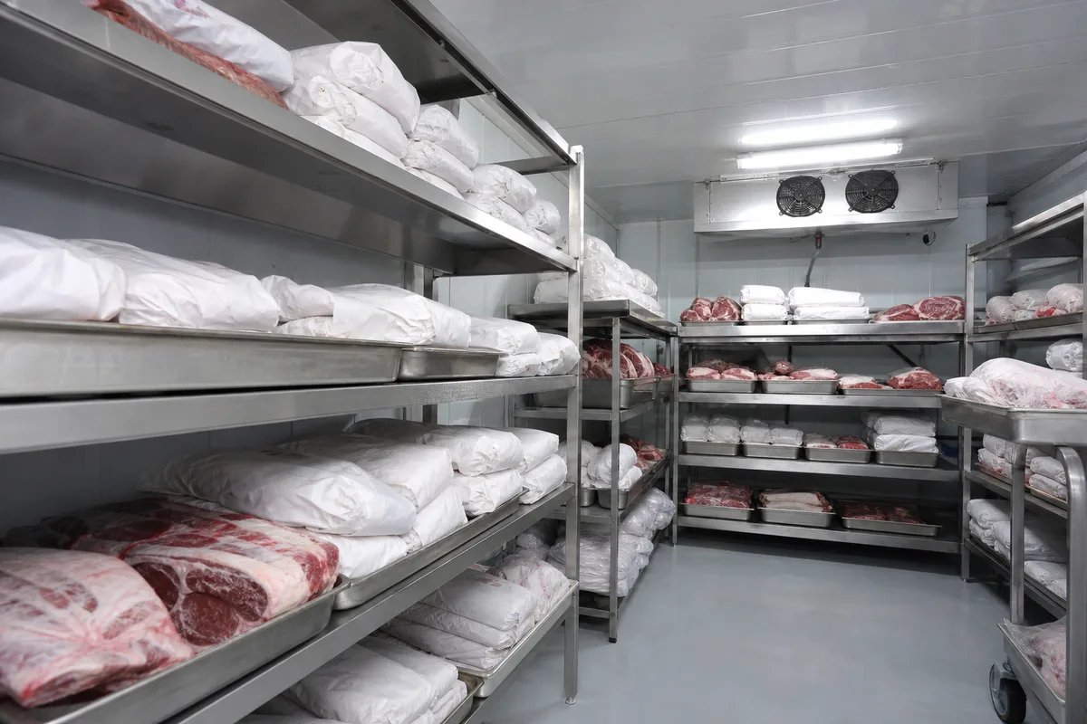 Chambre froide de boucherie avec commandes préparées et rangées sur des clayettes